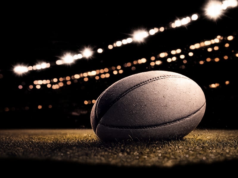 Rugby league ball on floodlit stadium turf at night.